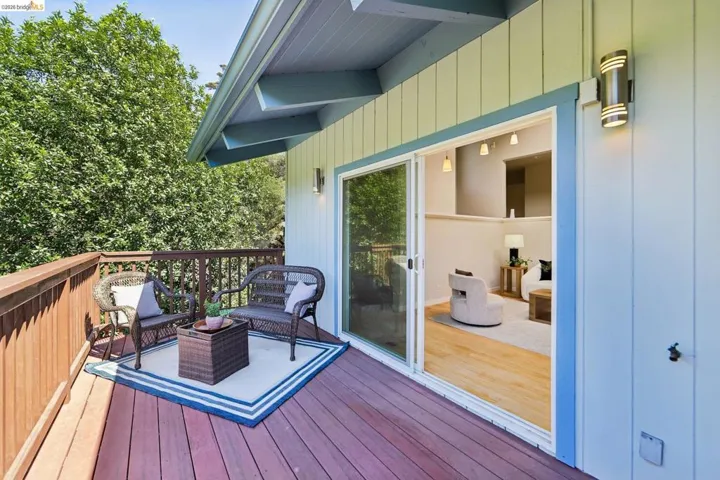 Exterior wood deck with natural wood railing, light green vertical siding, and a blue-trimmed sliding glass door