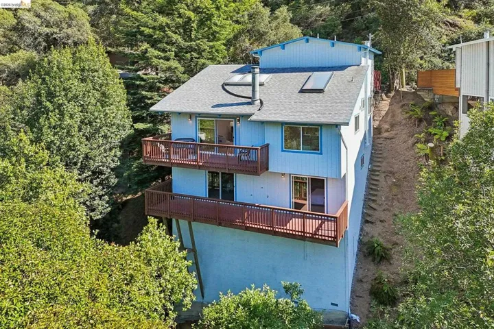 Multi-level residence featuring a light blue exterior, two spacious balconies with wood railings, a gray shingle roof, and multiple skylights