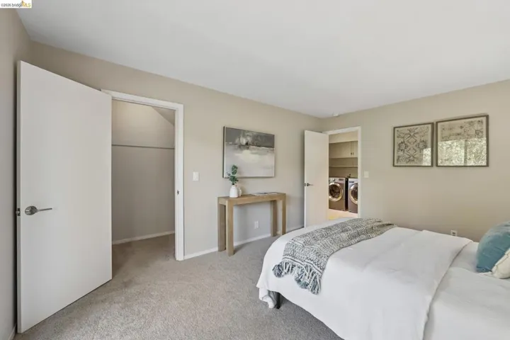 Carpeted room featuring a built-in closet with a hanging rod, a separate laundry area with front-load appliances and shelving, and contemporary light-colored walls