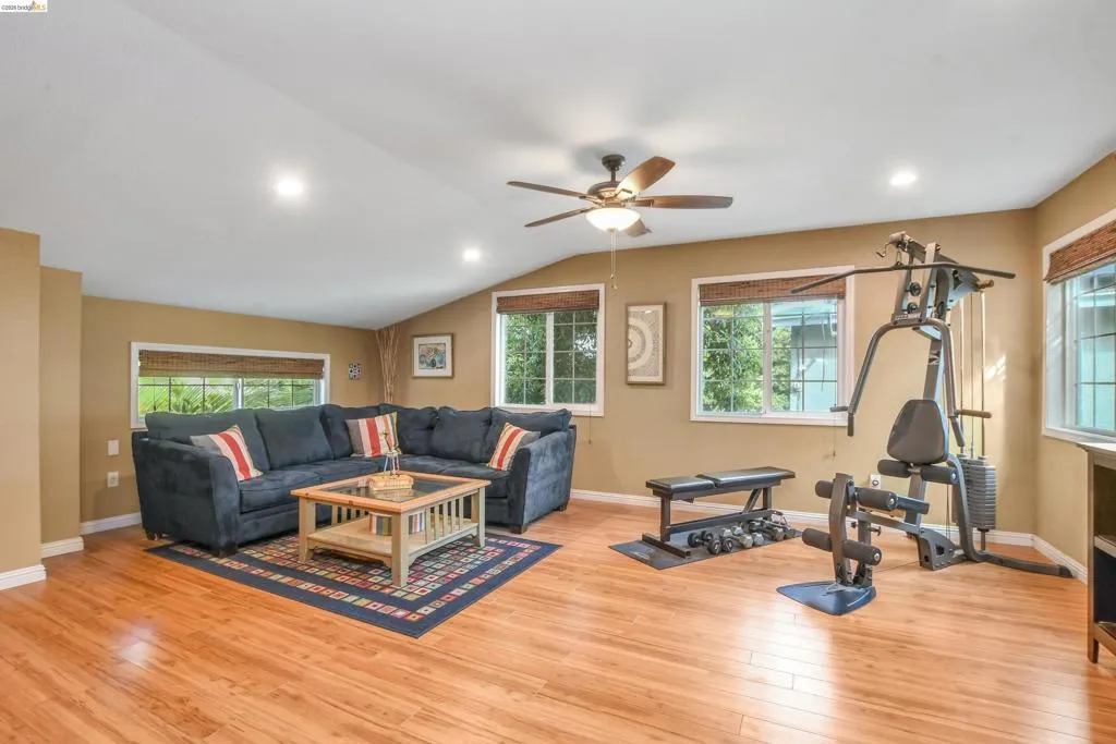 Spacious room featuring wood-finish flooring, multiple windows with blinds, recessed lighting, and a ceiling fan