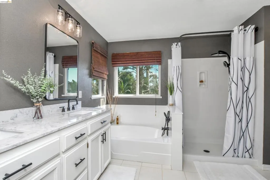Bathroom featuring a double vanity with white cabinetry and light-colored countertops, a freestanding bathtub, and a separate shower enclosure