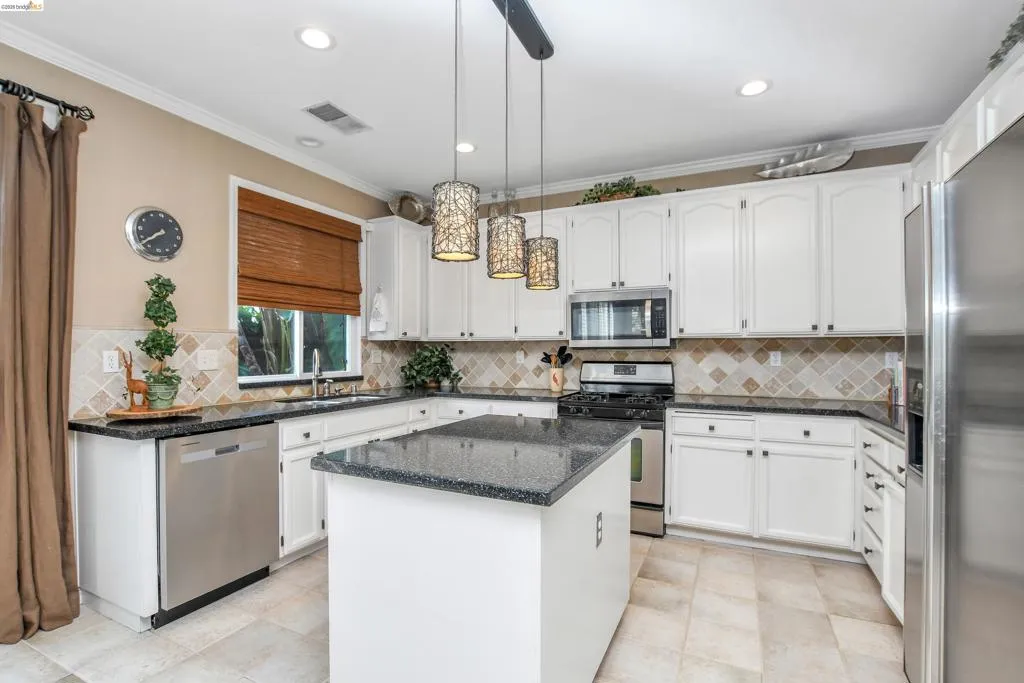 Kitchen featuring white cabinetry, dark stone countertops, stainless steel appliances, and a central island