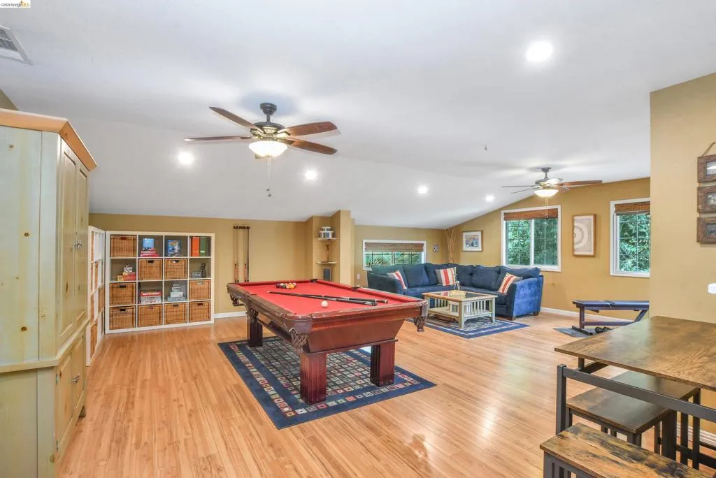Spacious recreation room featuring wood-finish flooring, vaulted ceilings with recessed lighting, and multiple ceiling fans