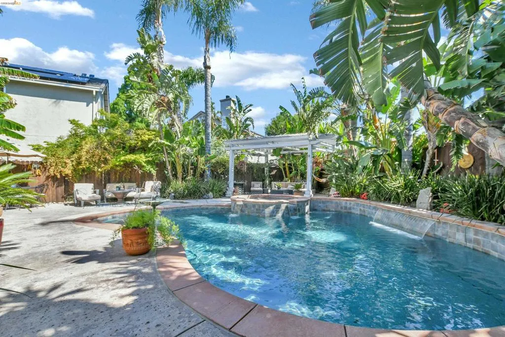 Curved swimming pool featuring a tiled waterline, integrated water features, and a surrounding paver patio
