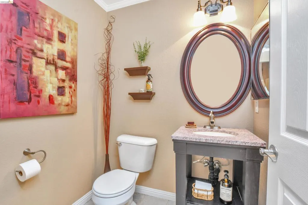 Bathroom featuring a corner vanity with a granite-style countertop, a white ceramic sink, and a framed oval mirror