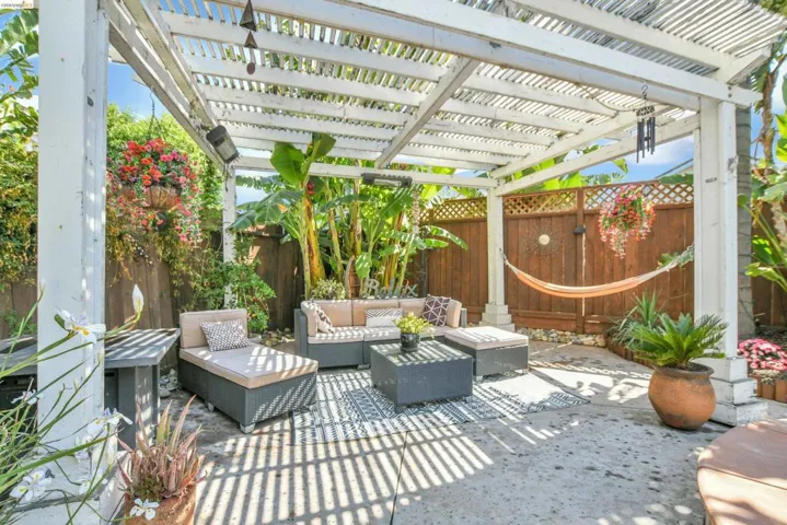 Paved patio area featuring a white slatted pergola, surrounded by wood fencing and lush greenery