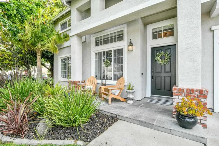 Front exterior featuring a paneled entry door with transom window, exterior sconce lighting, and a brick-accented column