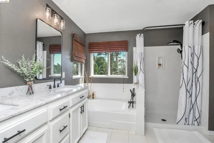 Bathroom featuring a double vanity with white cabinetry and light-colored countertops, a freestanding bathtub, and a separate shower enclosure