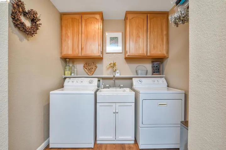 Dedicated laundry area featuring wood-finish flooring, light-toned walls, and wood cabinetry