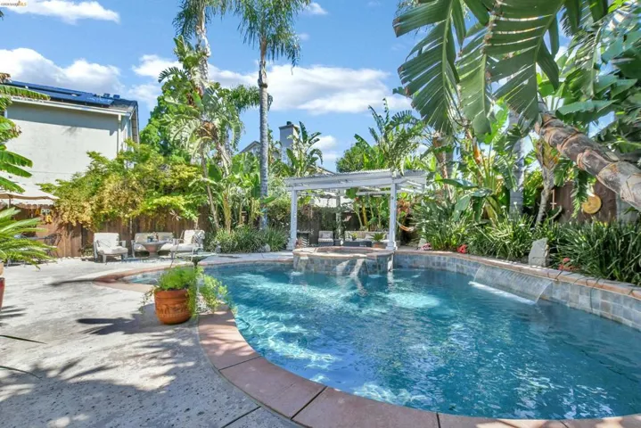 Curved swimming pool featuring a tiled waterline, integrated water features, and a surrounding paver patio