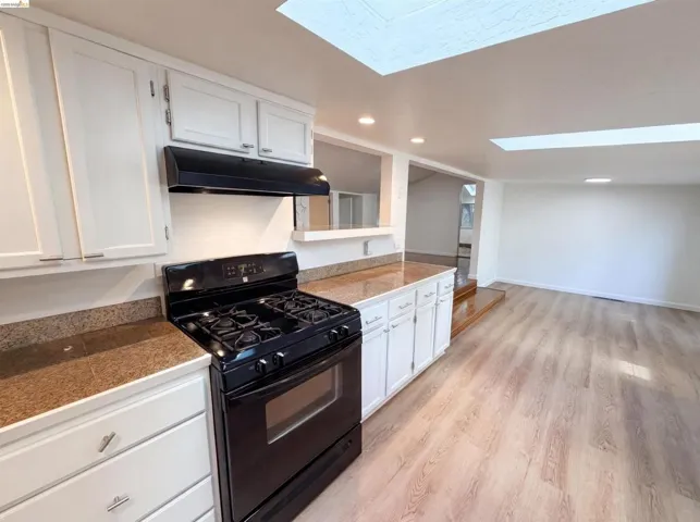 Kitchen featuring white cabinetry, a black range with an overhead vent, and speckled countertops