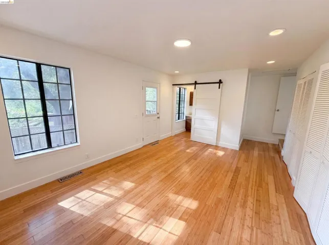 Spacious room featuring light wood-finish flooring, recessed lighting, and a white barn door
