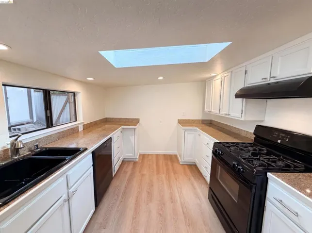 Kitchen featuring a skylight, wood-finish flooring, white cabinetry, integrated black appliances, and a double basin sink