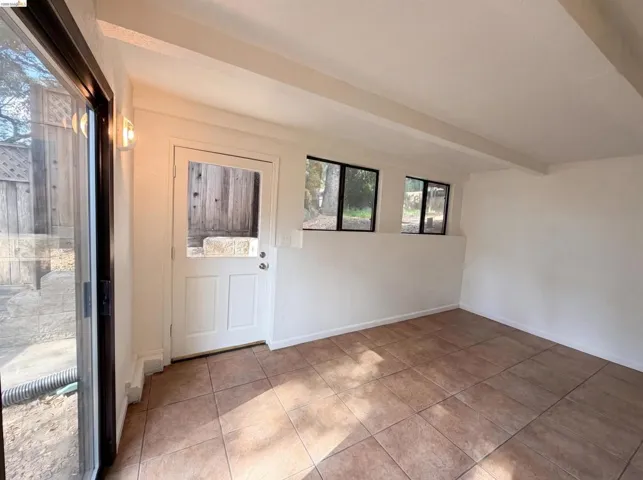 Spacious room featuring tile flooring, exposed ceiling beams, white walls, and multiple windows