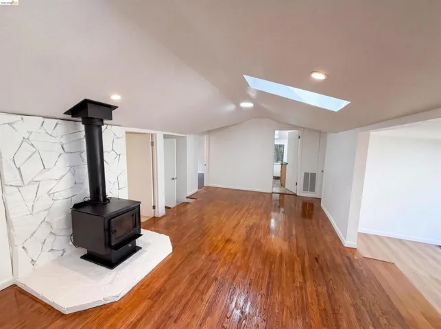 Living space featuring a prominent wood-burning stove with a white stone surround, rich wood-finish flooring, and a skylight for natural light