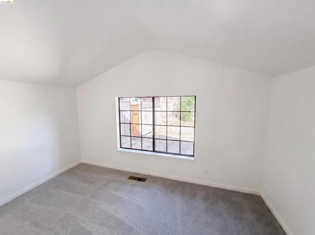 Vaulted ceiling bedroom with a grid-pattern window, light gray carpet, white walls, and white baseboards