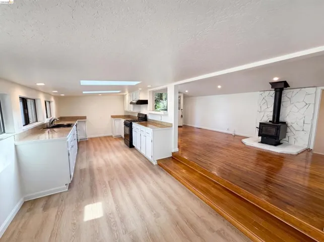 Open-concept kitchen and living area featuring wood-finish flooring, white cabinetry, dark appliances, and a skylight