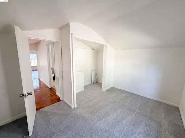 Carpeted room with white walls, an open doorway revealing a wood-finish floor beyond, and a built-in alcove