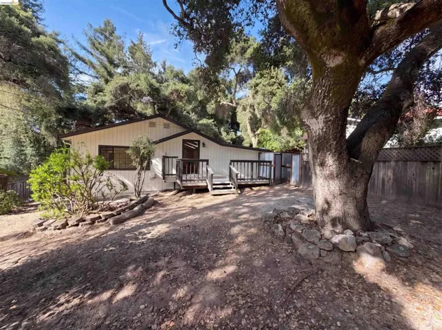 Expansive yard featuring a mature tree with rock surround, board and batten siding, multiple windows, a wooden deck, and a privacy fence