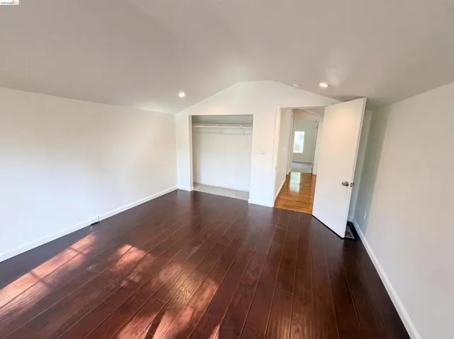 Room featuring dark wood-finish flooring, white walls, and a vaulted ceiling with recessed lighting
