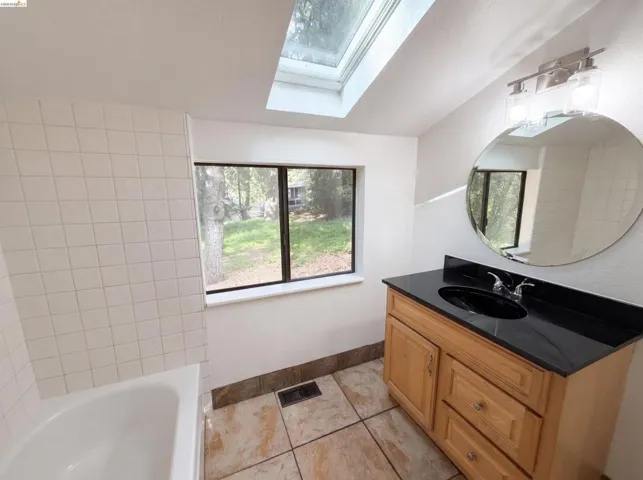 Bathroom featuring a light wood-finish vanity with a black countertop and oval sink, a round wall mirror, and a two-bulb vanity light fixture