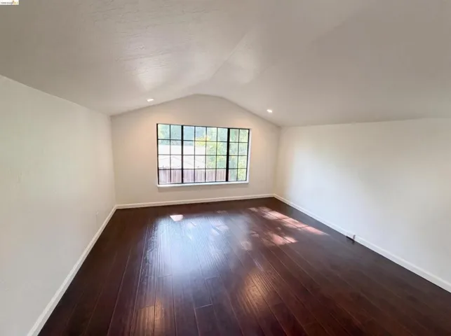 Interior room featuring dark wood-finish flooring, white walls, and a vaulted ceiling with recessed lighting
