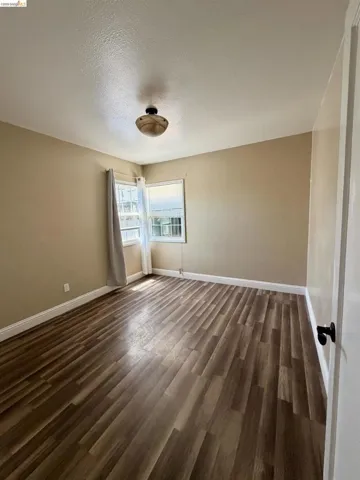Spacious room featuring wood-finish flooring, neutral-toned walls, and a ceiling-mounted light fixture