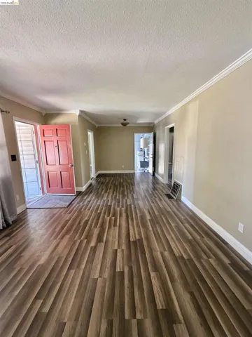 Expansive living area featuring wood-finish flooring, neutral wall tones, white crown molding, and a red front door