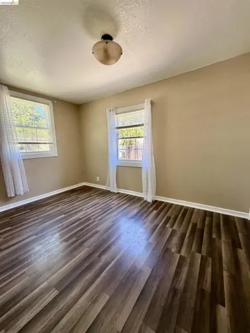 Spacious interior room featuring wood-finish flooring, two windows with white trim, and light beige walls