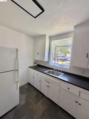 Kitchen featuring a stainless steel sink, dark countertops, white cabinetry, slate-look floor tiles, and a window