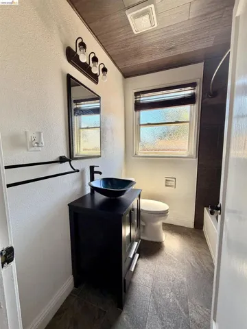 Bathroom featuring a vessel sink with a dark wood-finish vanity, recessed lighting, a window with blinds, and dark tile flooring