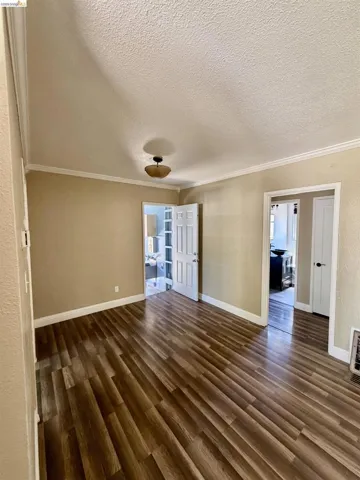 Spacious room with wood-finish flooring, neutral-toned walls, white baseboards, and crown molding