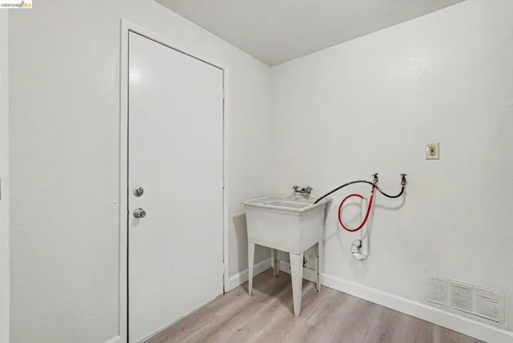 Utility room featuring a freestanding utility sink with dual faucets, wood-finish flooring, and white painted walls