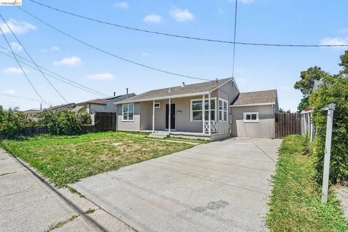 Single-story residence featuring a covered front porch with decorative railing, an enclosed sunroom with multiple windows, and a detached garage structure