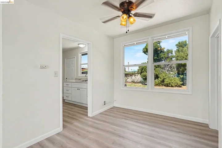Spacious room with light wood-finish flooring, white walls, and a ceiling fan with integrated lighting