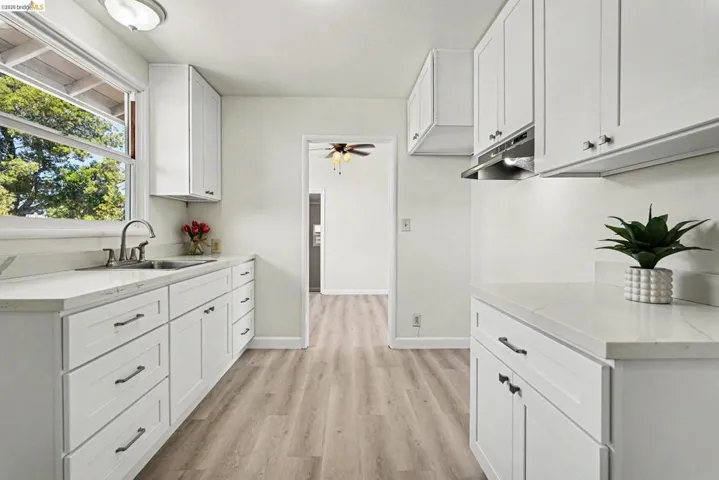 Kitchen featuring white shaker-style cabinetry, light-toned countertops, a stainless steel sink with a gooseneck faucet, and wood-finish flooring