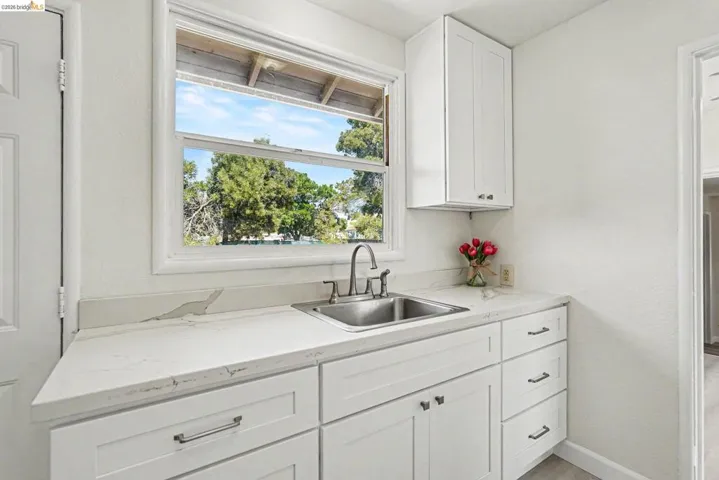 Bright utility space featuring a stainless steel sink with a chrome faucet, white shaker-style cabinetry, and light-toned countertops with veining