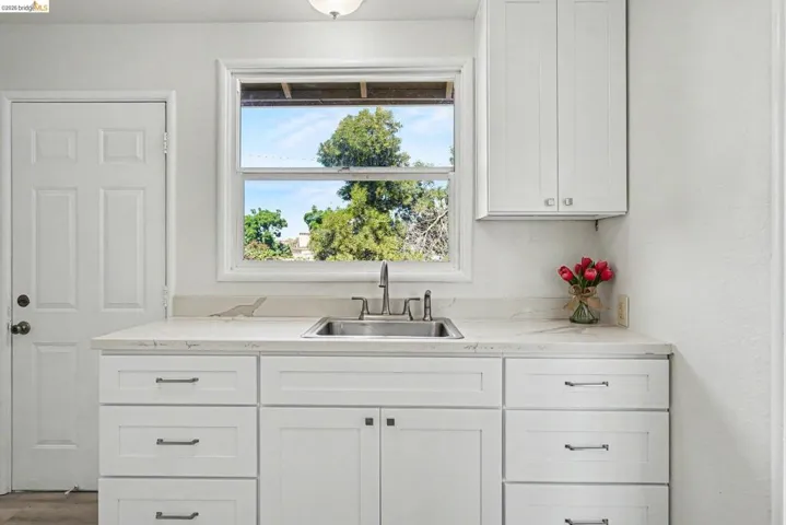 White cabinetry with dark hardware, a stainless steel sink, and light-toned countertops