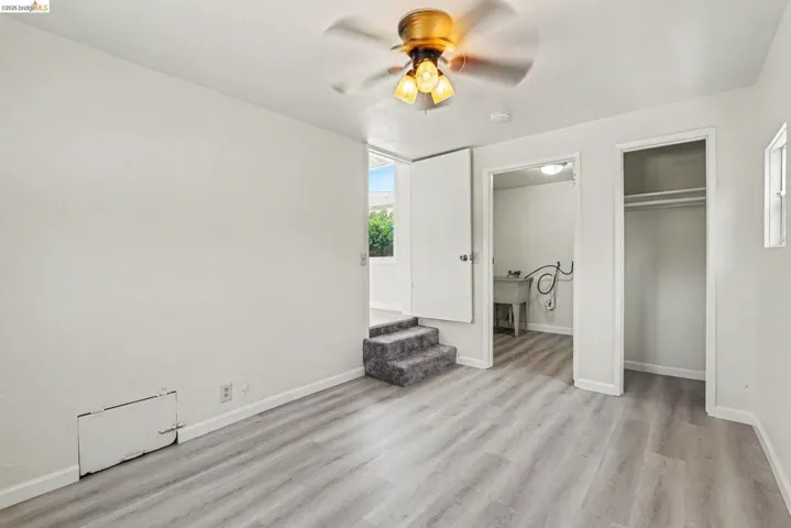 Interior space featuring wood-finish flooring, white walls, and a ceiling fan with integrated lighting