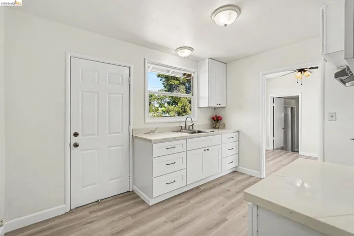 Kitchen featuring white cabinetry, light-toned countertops, a stainless steel sink, and wood-finish flooring