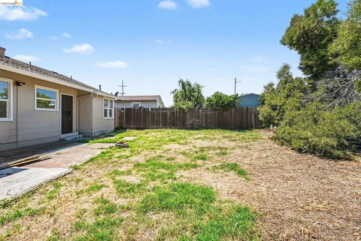 Expansive backyard featuring a partial patio, mature perimeter trees, and a full wood fence
