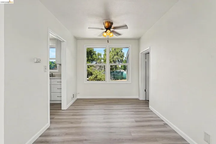 Bright interior space with wood-finish flooring, white walls, and a ceiling fan with integrated lighting