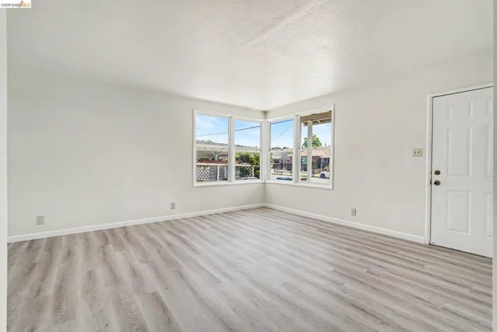 Bright living space featuring wood-finish flooring, white baseboards, and a prominent corner window configuration