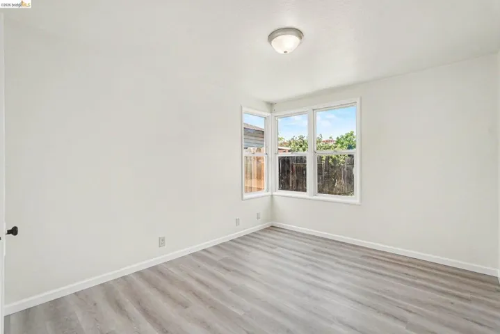 Bright room featuring a corner window configuration, light wood-finish flooring, white baseboards, and a semi-flush mount ceiling light