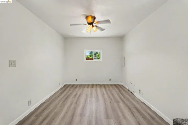 Room featuring wood-finish flooring, white walls, a window, a ceiling fan, and white baseboards