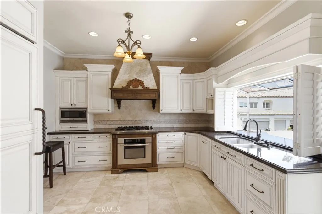 Mediterranean style kitchen with panel front refrigerator, 6 burner gas cook top, oven (new oven not shown) and shutters opened to greenhouse window behind sink.