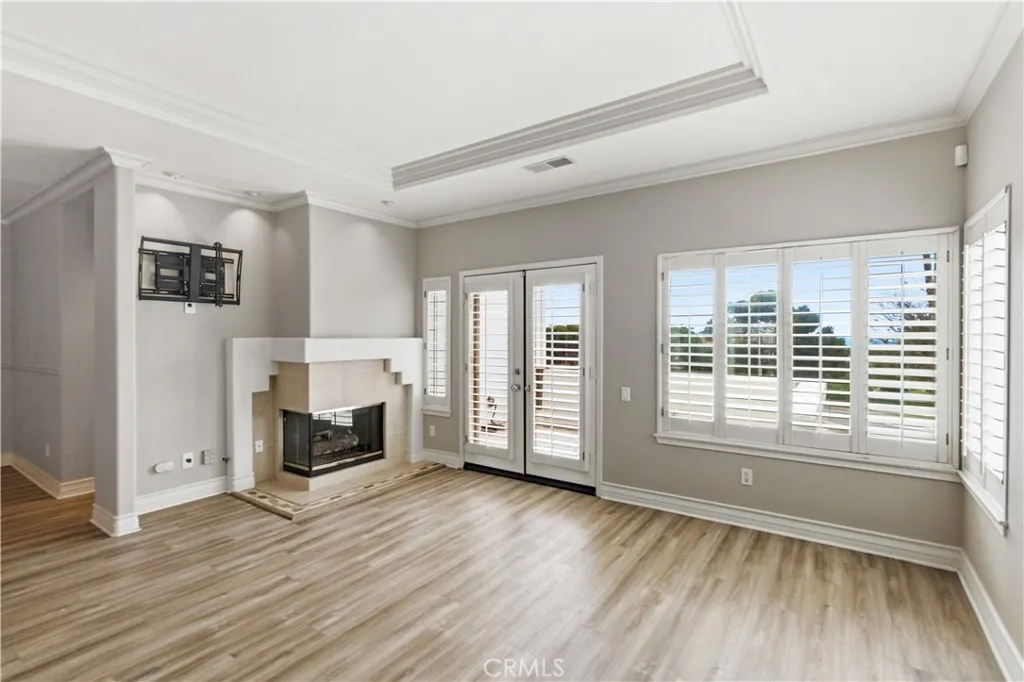 Living room with corner gas fireplace, TV mount, french doors to balcony with ocean view, tray ceiling, plantation shutters