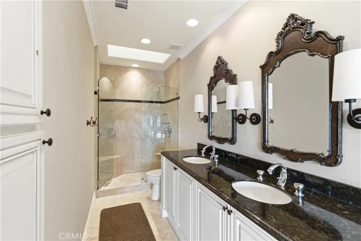 Primary en suite bathroom - travertine shower with skylight, granite counter / dual sinks, and linen cabinet
