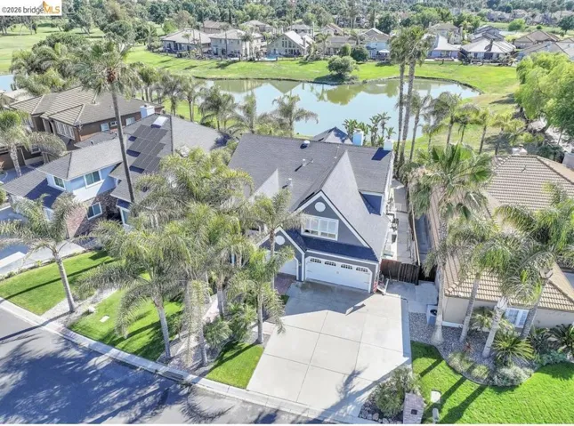 Contemporary residence with a dark-pitched roof and light-blue siding, featuring a two-car garage, mature palm trees, a concrete driveway, and solar panels