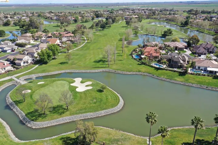 Aerial perspective showcasing a golf course community with a prominent island green, surrounding water features, and manicured fairways
